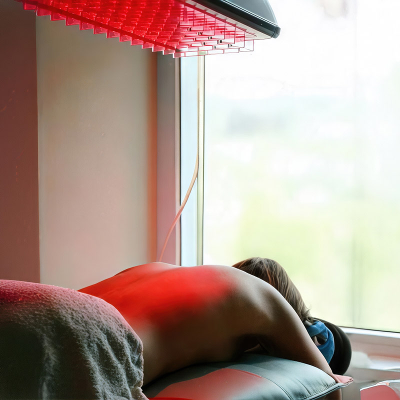 Eine Frau liegt auf einer Therapieliege und wird mit einem Heuser Rotlichtstrahler behandelt